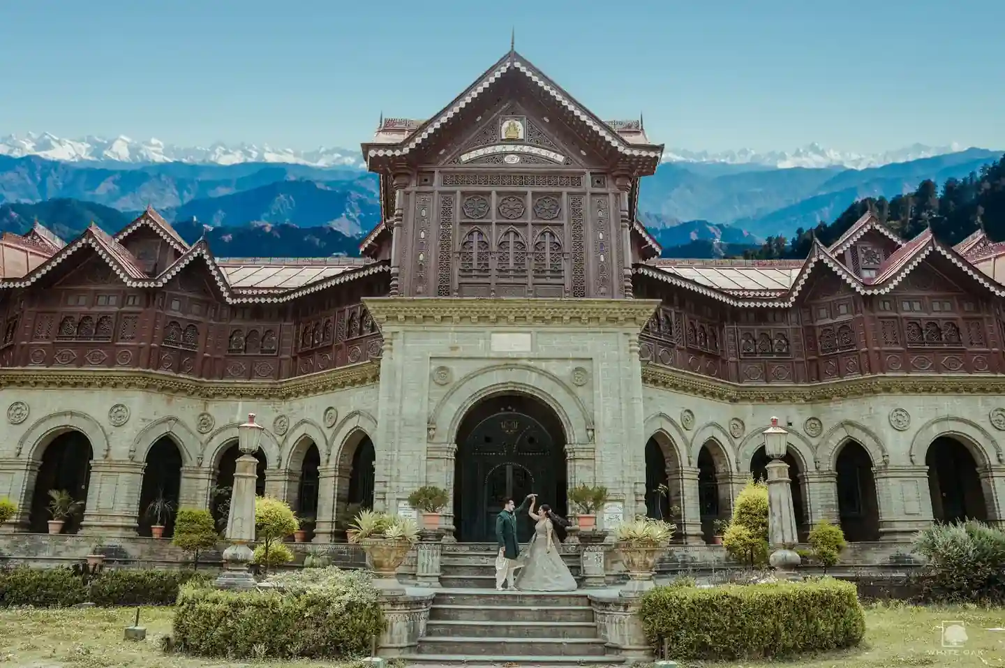 Couple posing in front of a grand heritage building with mountains in the background